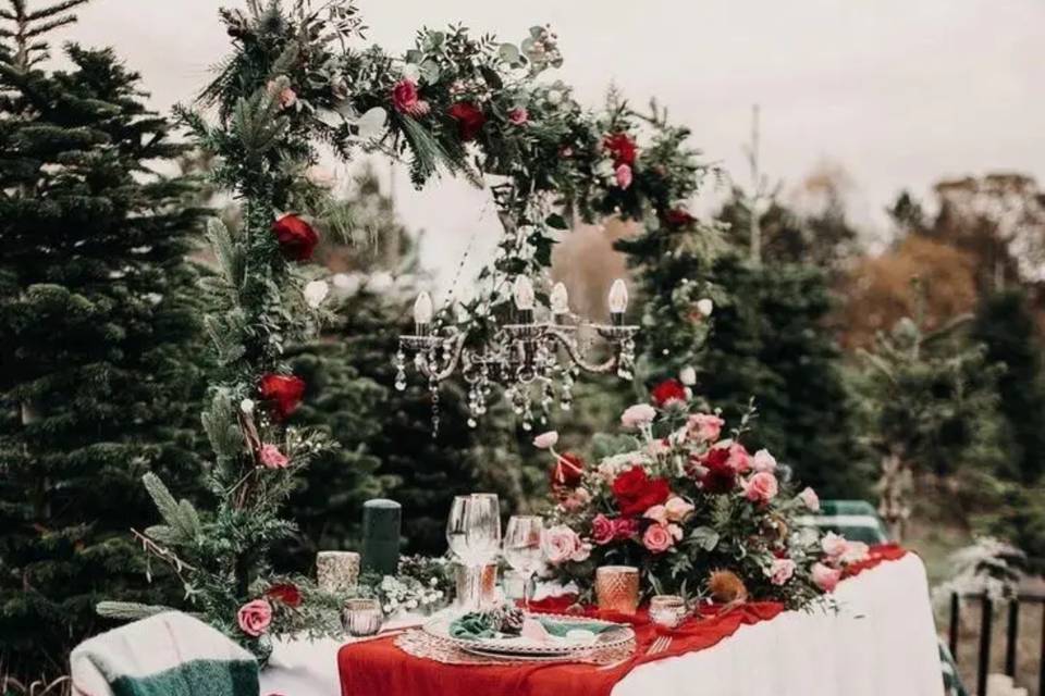 festive table set up with a large floral wedding centerpiece, hanging chandelier and floral arch