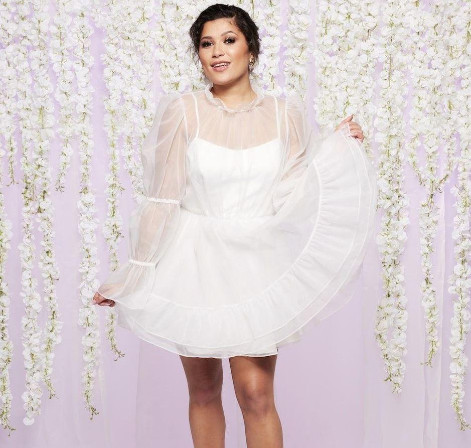 MAFS uk contestant tasha wears a white tulle dress in front of a purple backdrop with white hanging flowers