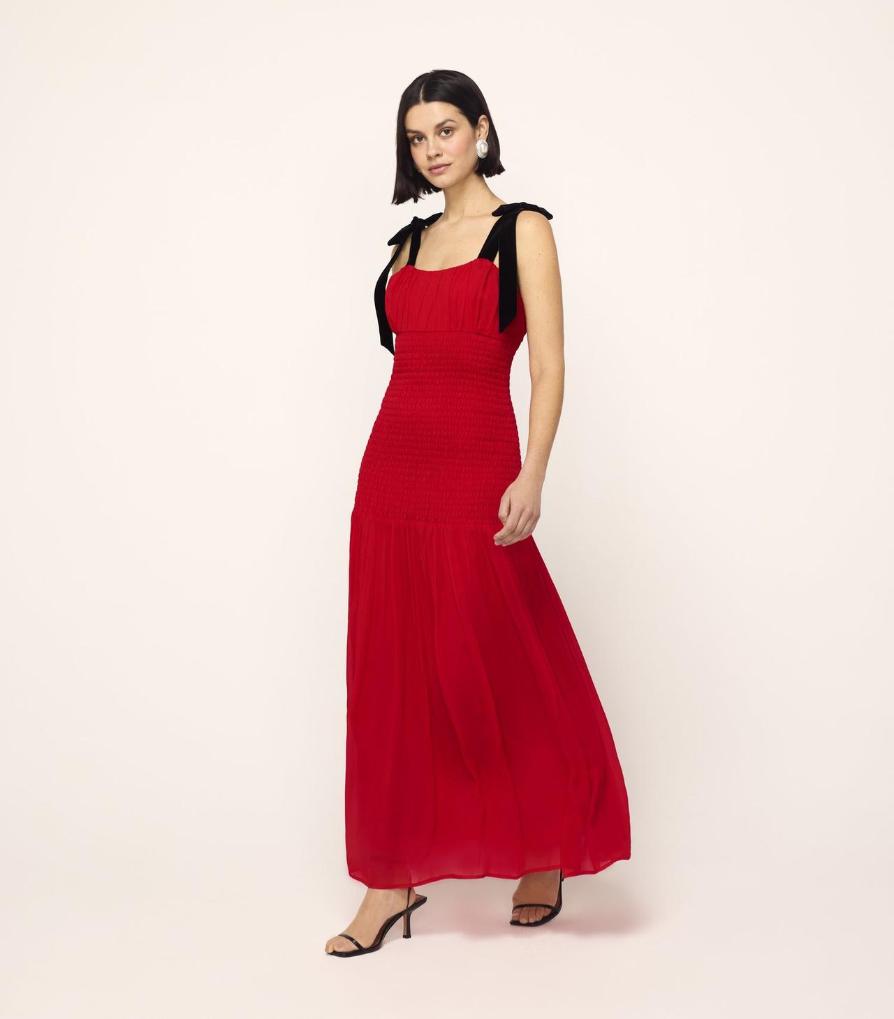 A wedding guest wearing a red shirred maxi dress with black velvet tie straps and black sandals.