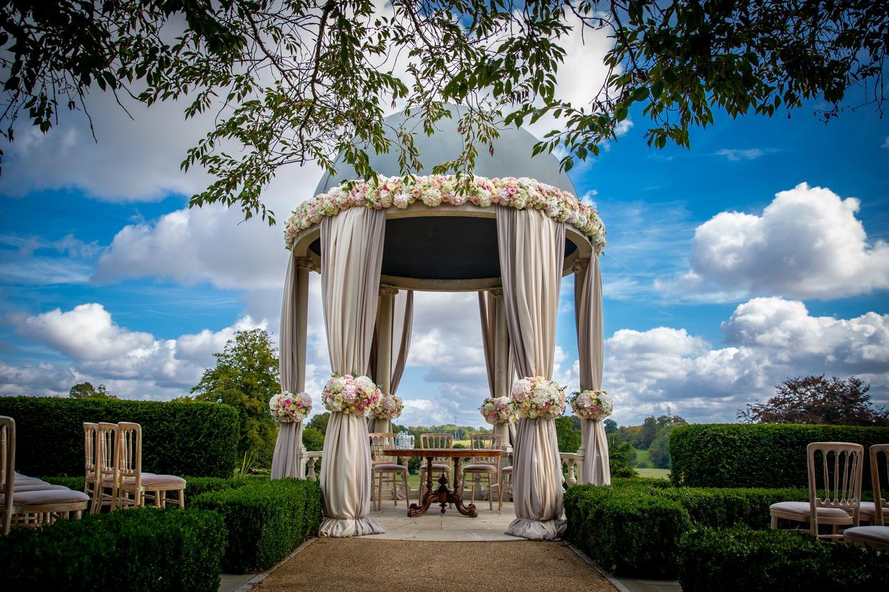 Outdoor ceremony area featuring a grand stone dome dressed in drapes and flowers.