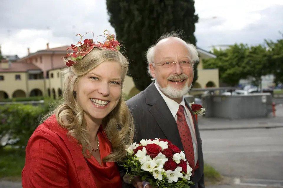 A bride dressed in read smiles at the camera accompanied by her father