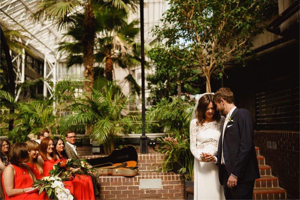 couple saying their vows in The Barbican's conservatory surrounded by guests and owering greenery