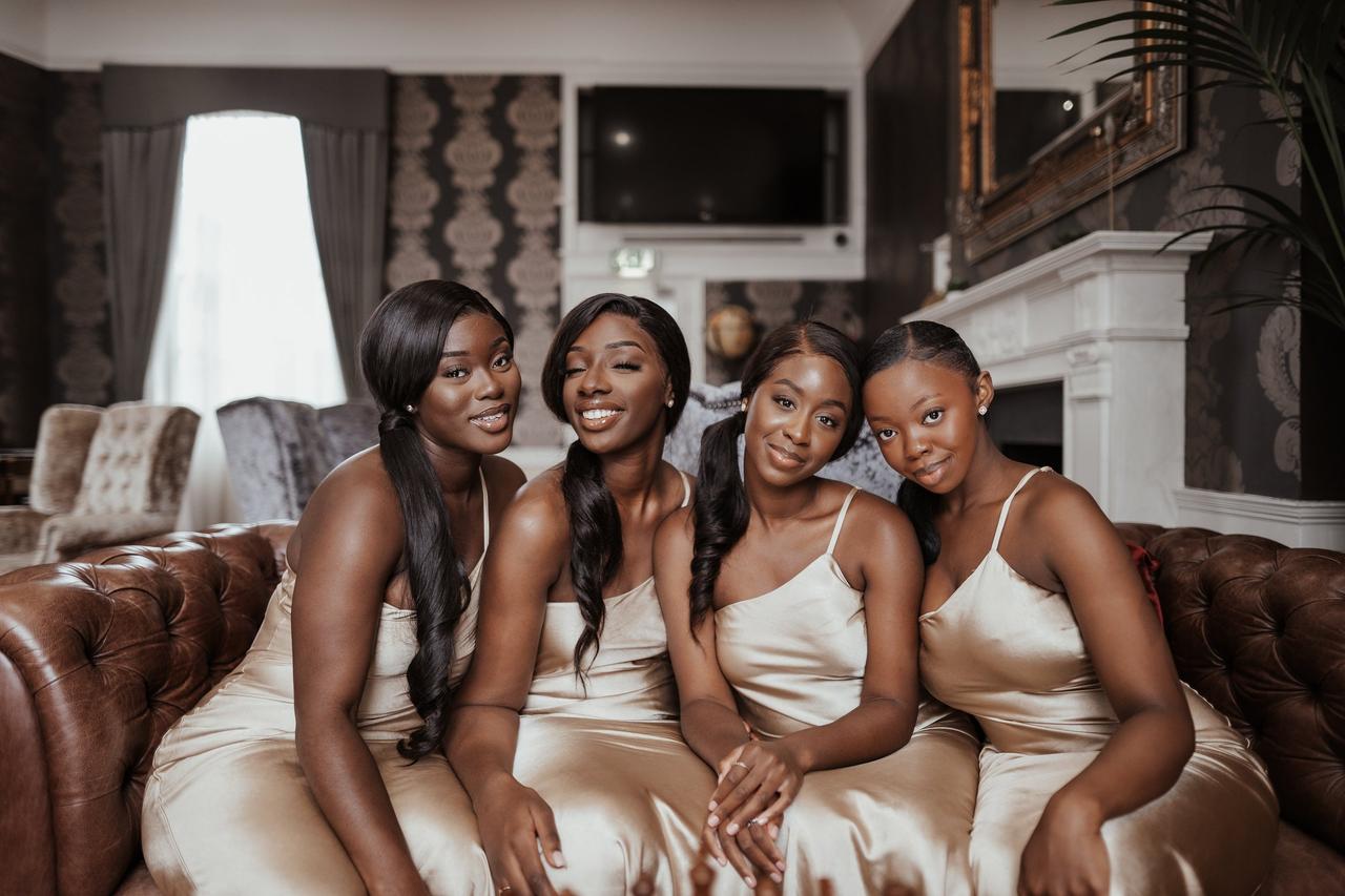 Four bridesmaids in satin bridesmaid dresses sitting on a sofa posing together