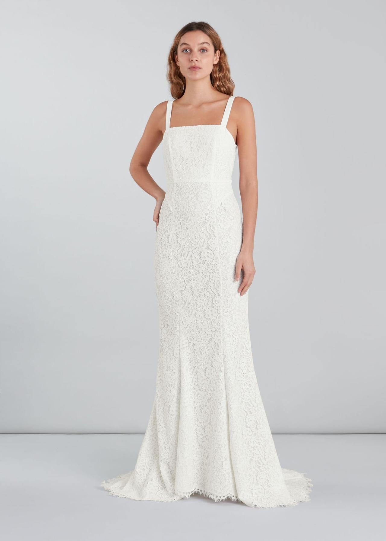 White woman with wavy dark blonde hair wearing a sleek lace wedding dress with a square neckline