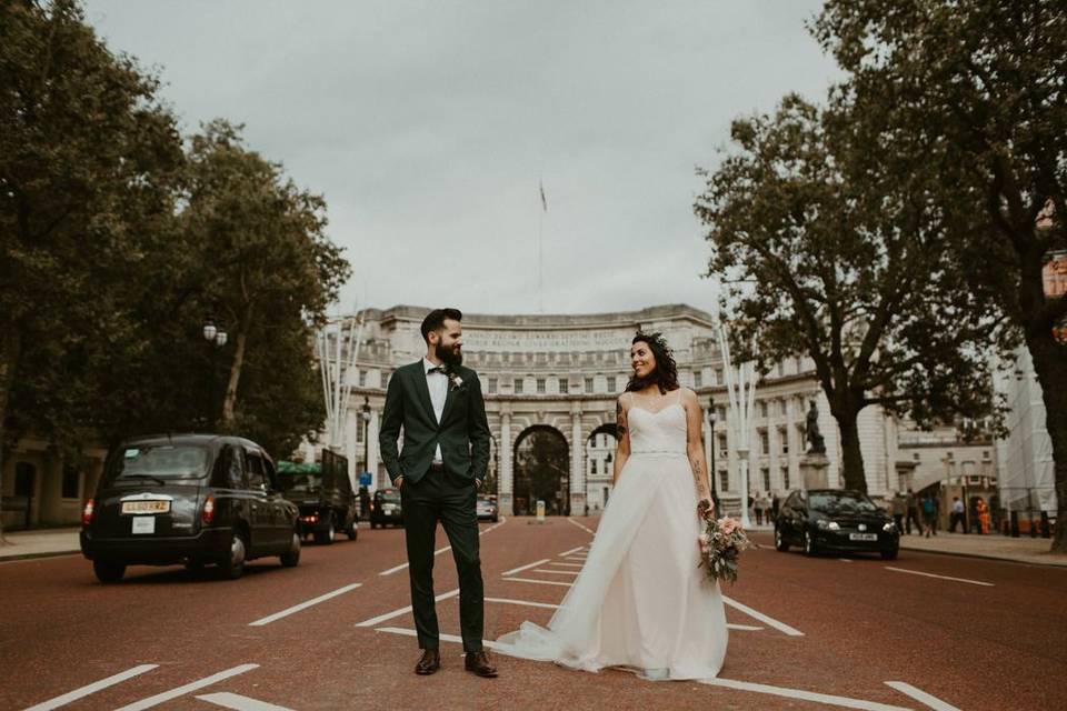 Bride and groom stand in the road beside St James's Park in front of a white marble structure