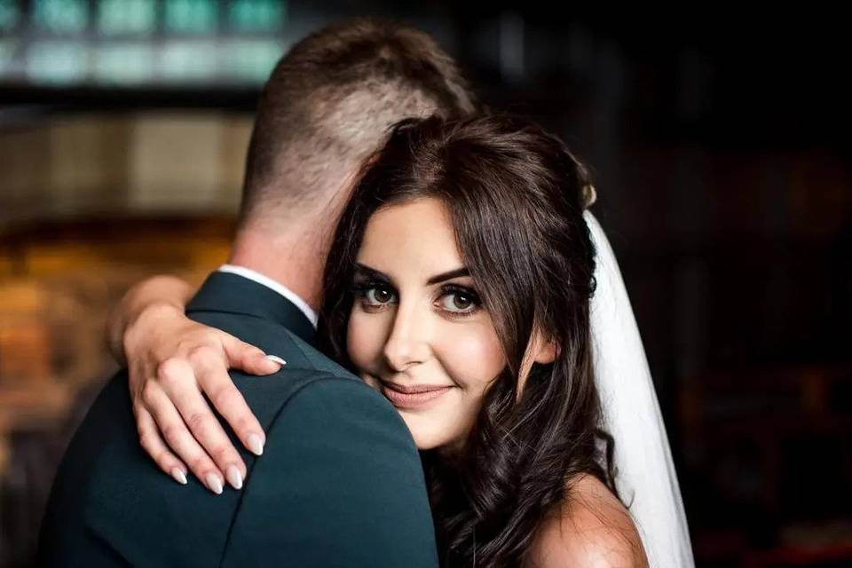 Bride with natural looking wedding makeup and dark hair, embracing a man whose face can't be seen