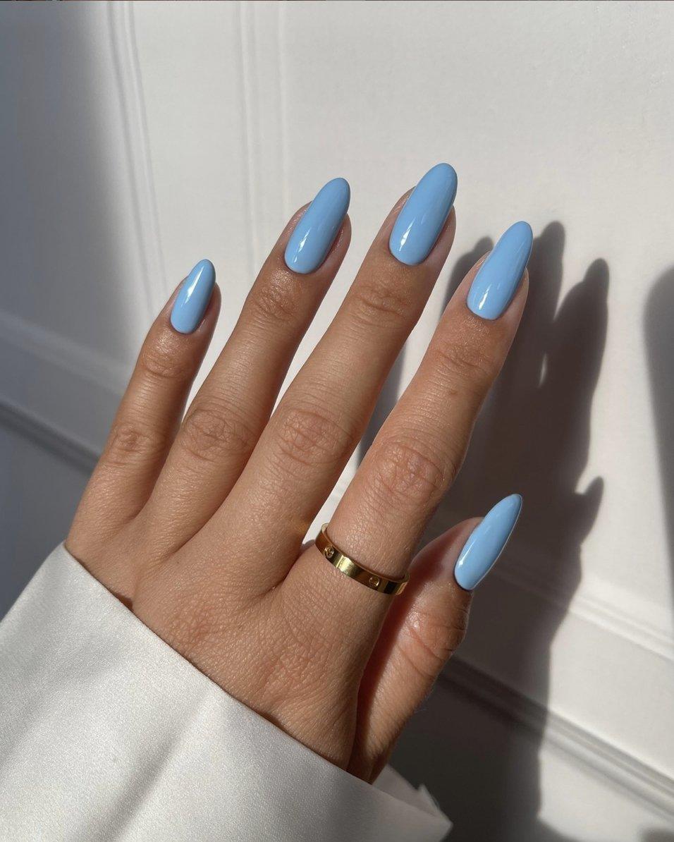 Close up of white woman's hand with a white sleeve wearing a sky blue manicure and gold diamond studded ring on her index finger