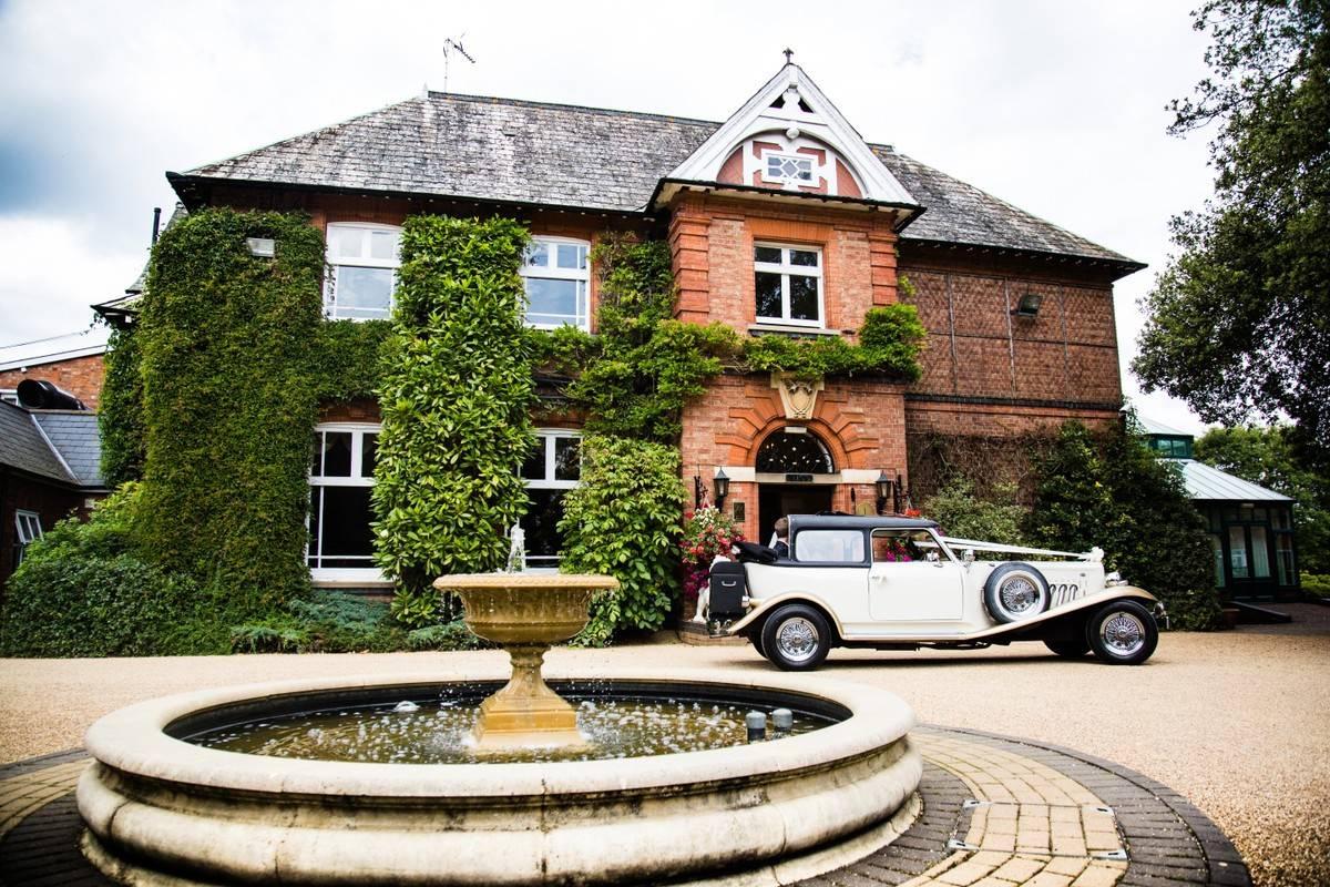 Outside of a manor wedding venue with a classic car and water fountain