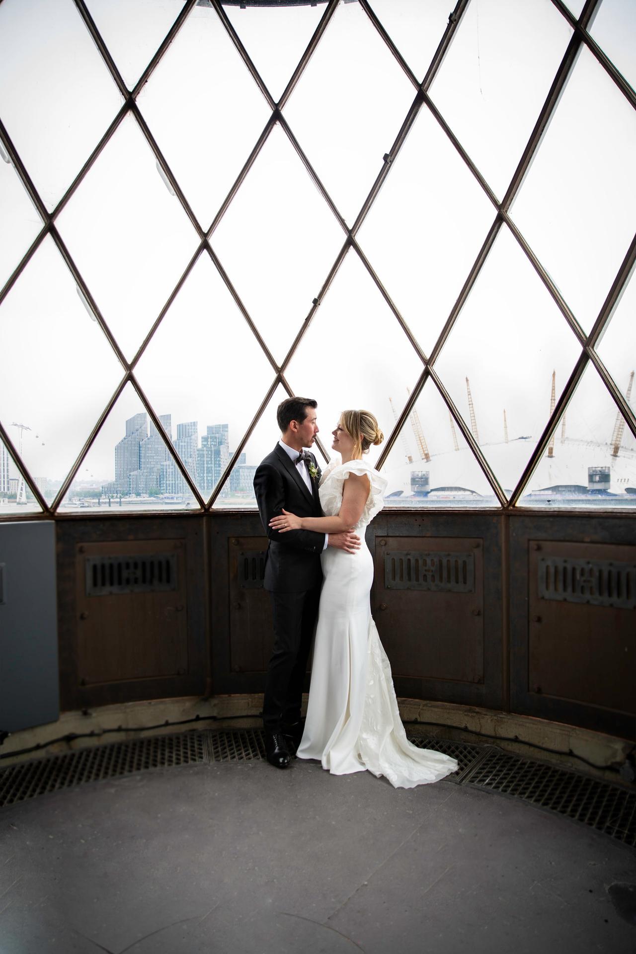 A bride and groom stand at the top of a lighthouse holding each other