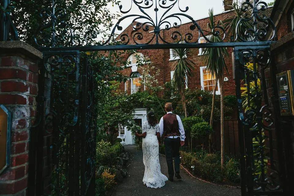 Newlyweds hold hands in the lush gardens of a stately wedding venue