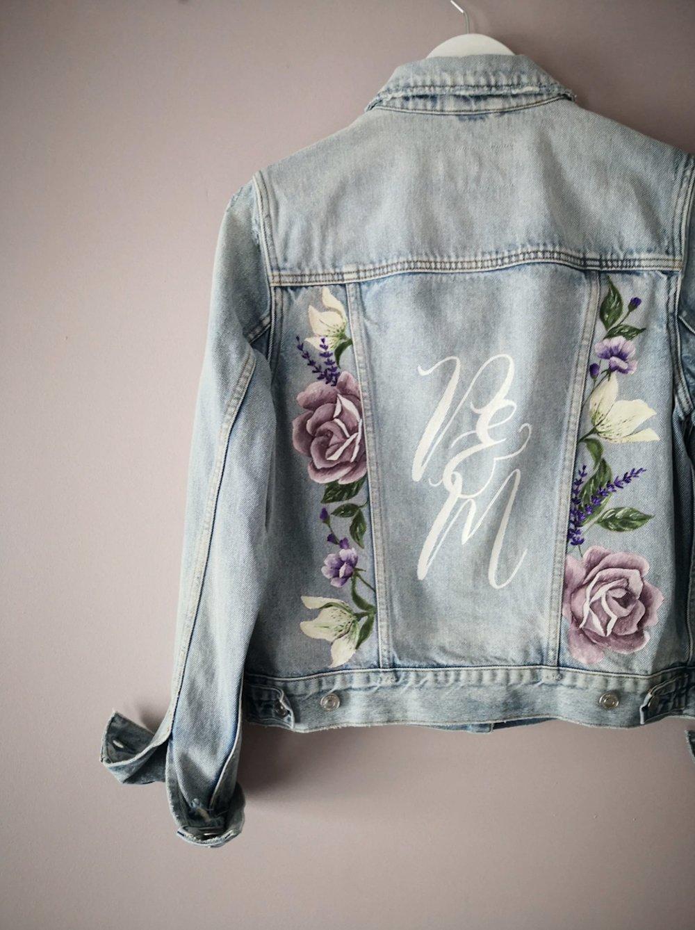 Light blue denim jacket with 'P & M' and purple and green florals painted onto the back