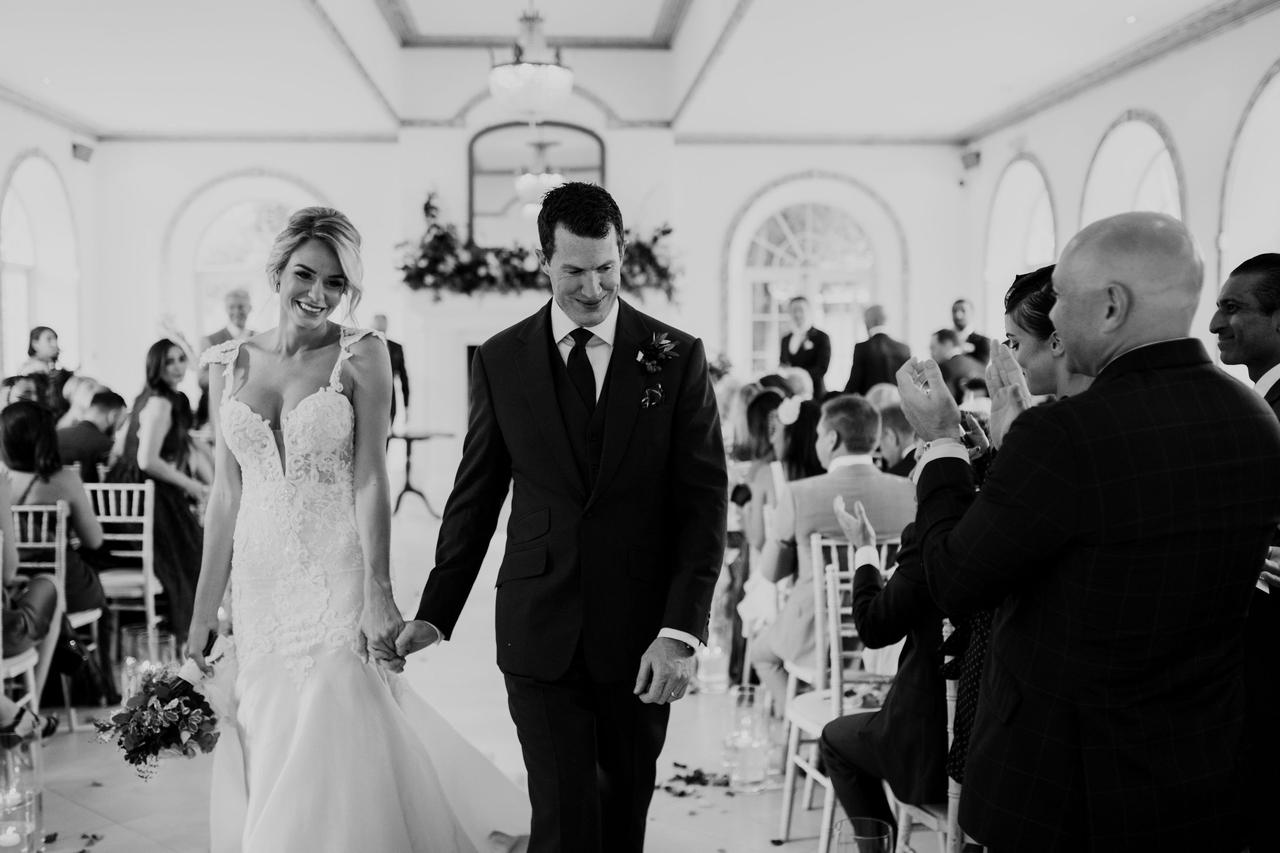 Black and white photograph of a bride and groom walking down the aisle