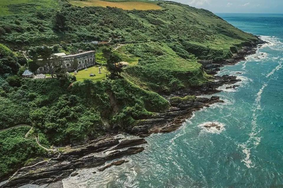 Aerial view of the Polhawn Fort wedding venue surrounded by lush forests and overlooking the ocean