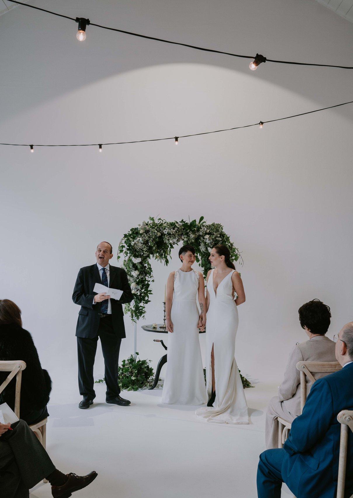 The brides hold hands at the top of the aisle