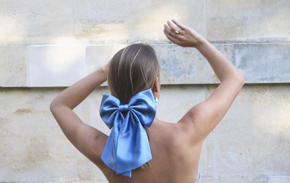 Tanned woman with highlights wearing a strapless top photographed from behind with her hair tied into a large blue silk bow