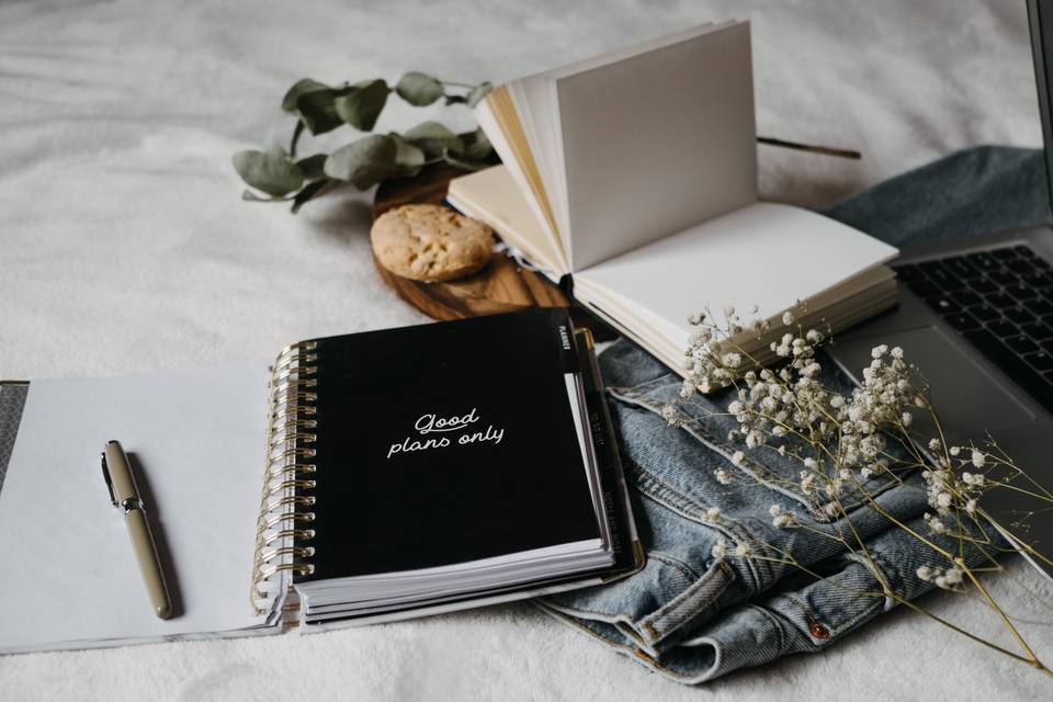 Notebook, pens and a laptop on a bed