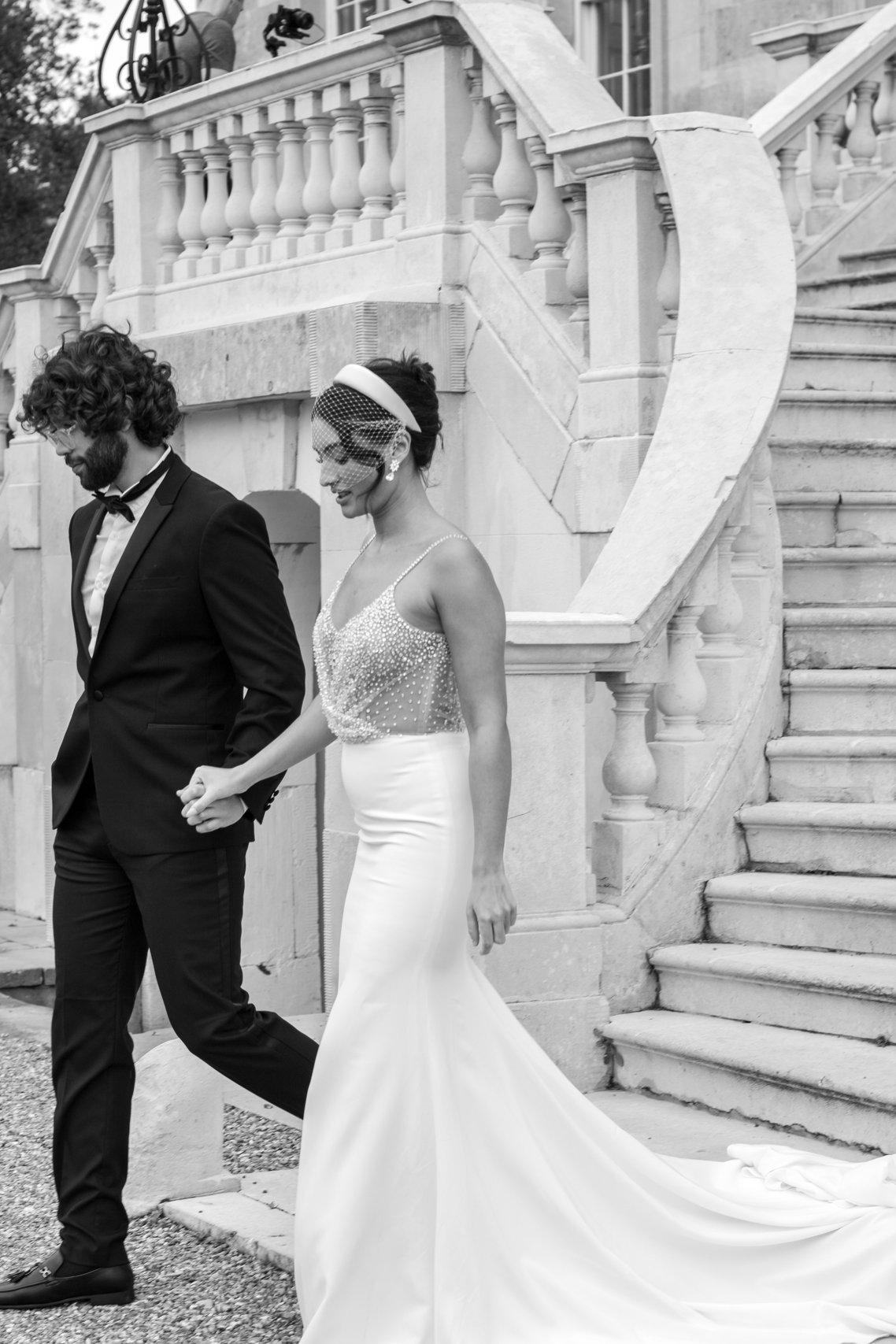 Black and white moody image of a bride and groom walking away from a venue