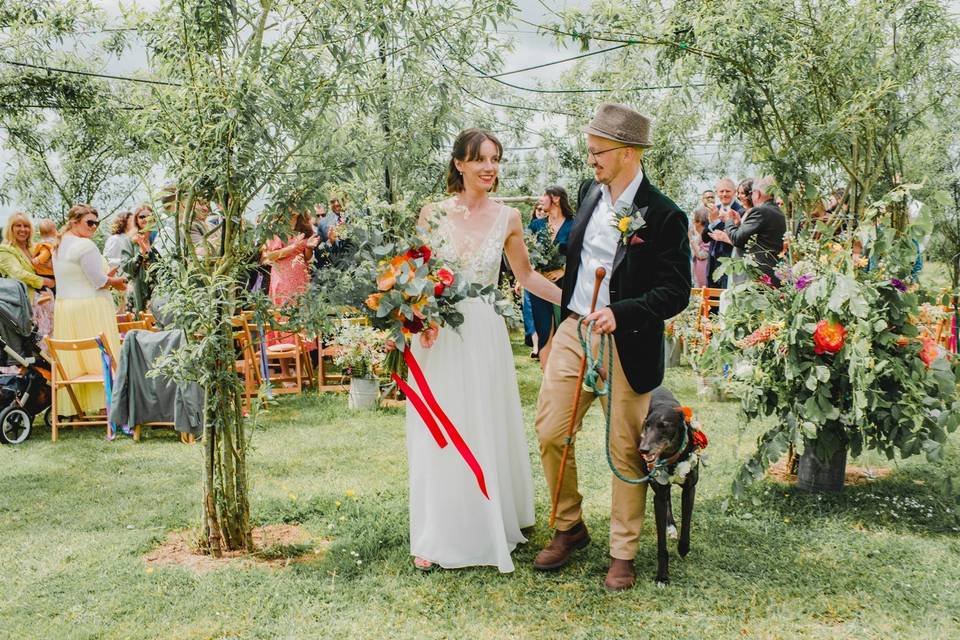 A bride and groom having a festival wedding in a wild garden surrounded by guests beneath a canopy of flowers