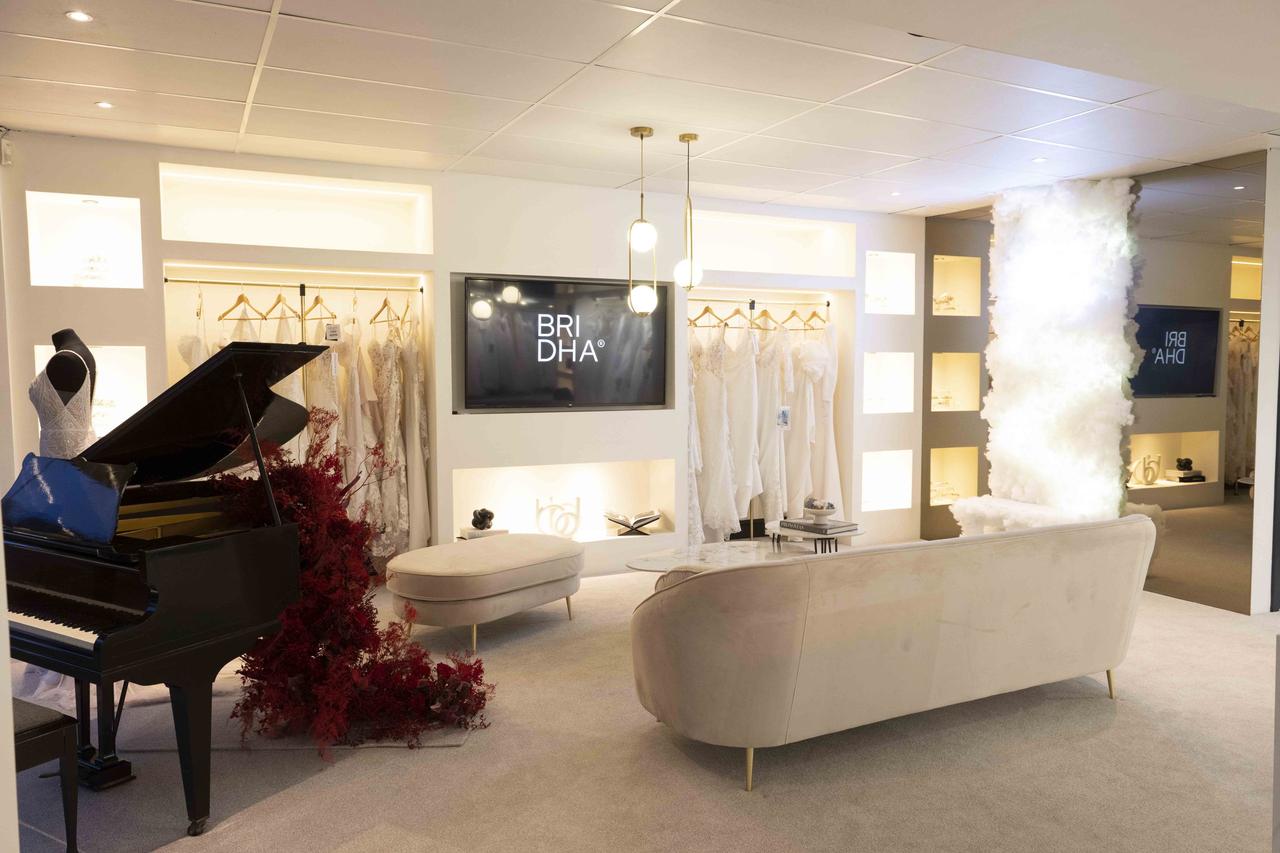 Interior of wedding shop BRIDHA featuring a white chaise lounge, a grand piano and dresses on rails