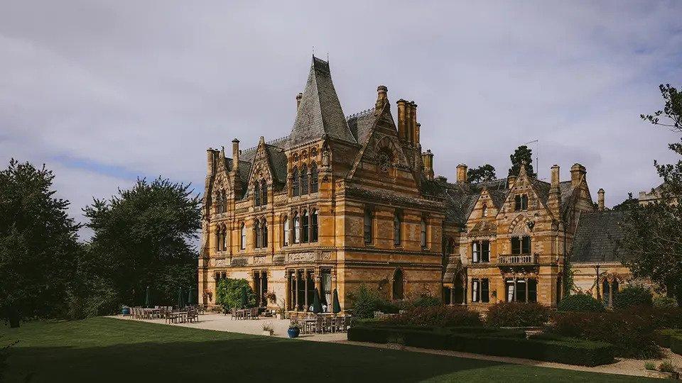 Exterior of Ettington Park Hotel surrounded by trees with chairs and tables set up outside