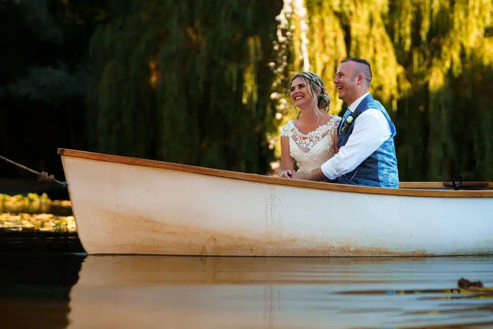 bride and groom sail in a rowing boat by some trees on a sunny day