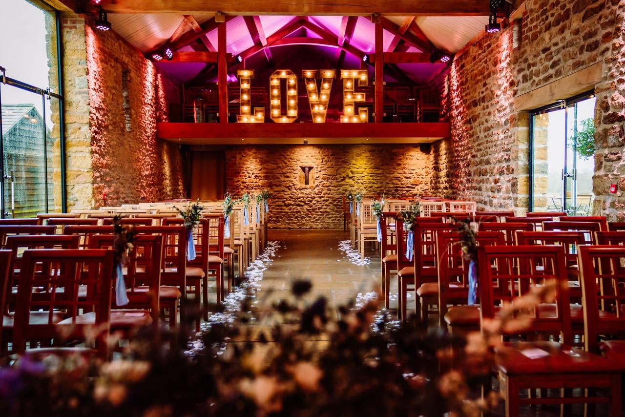 Rustic wedding ceremony space in a barn, with illuminated light up LOVE letters