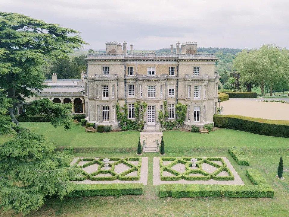 Drone shot of Hedsor House, a grey brick country house building with manicured gardens surrounded by trees