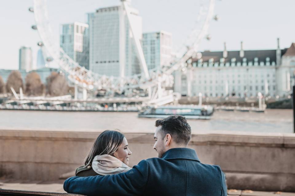 a couple with their arms around each other whilst on a london date with the london eye in the background