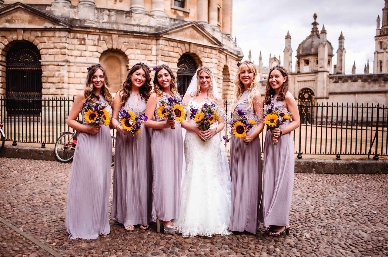 The bride poses in the middle of her bridesmaids carrying sunflower bouquets