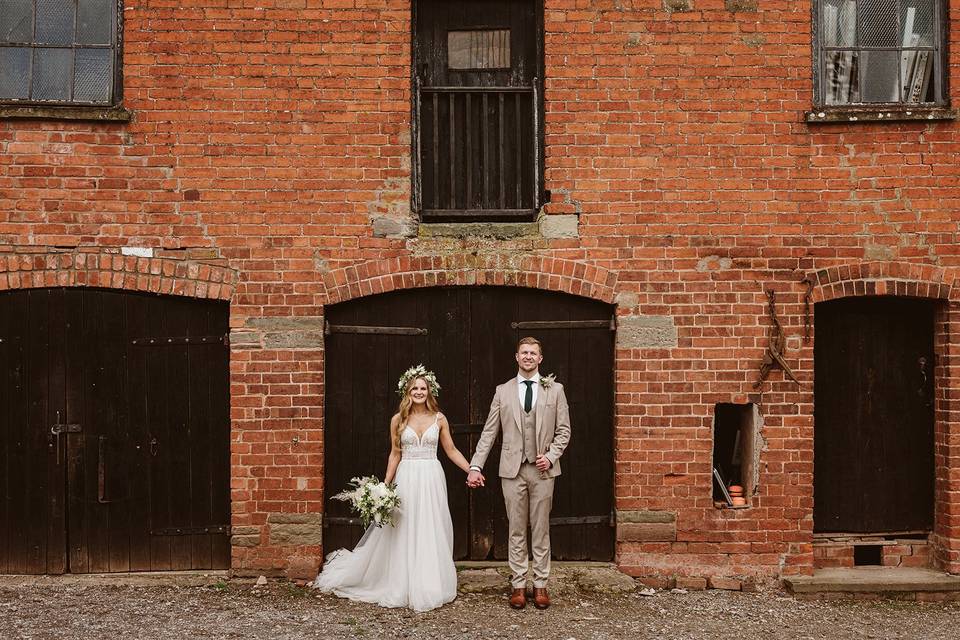 Bride and groom holding hands in front of a red brick farm building