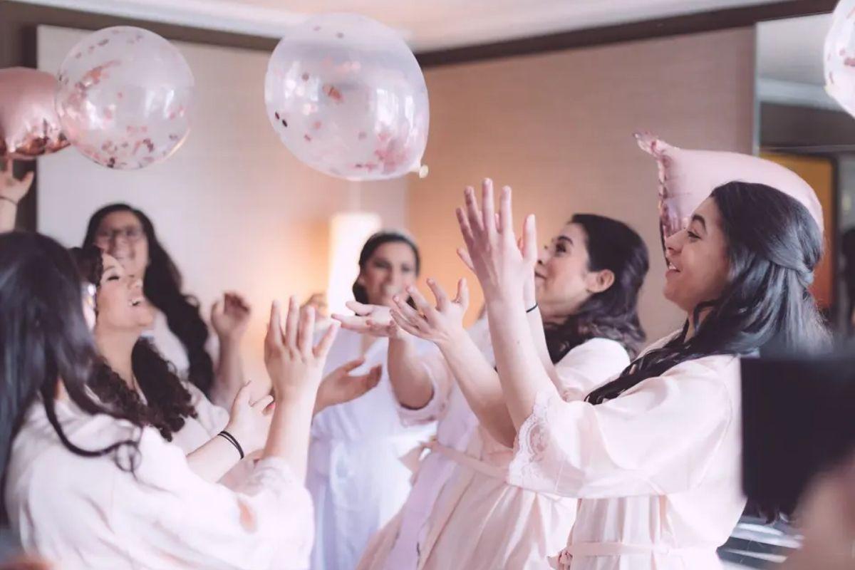 a bride and her four bridesmaids in matching white and pink robes playing with confetti balloons on the morning of the wedding