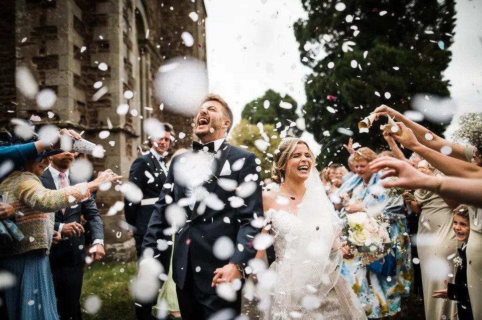 Bride and groom laughing with joy as guests pour confetti over them