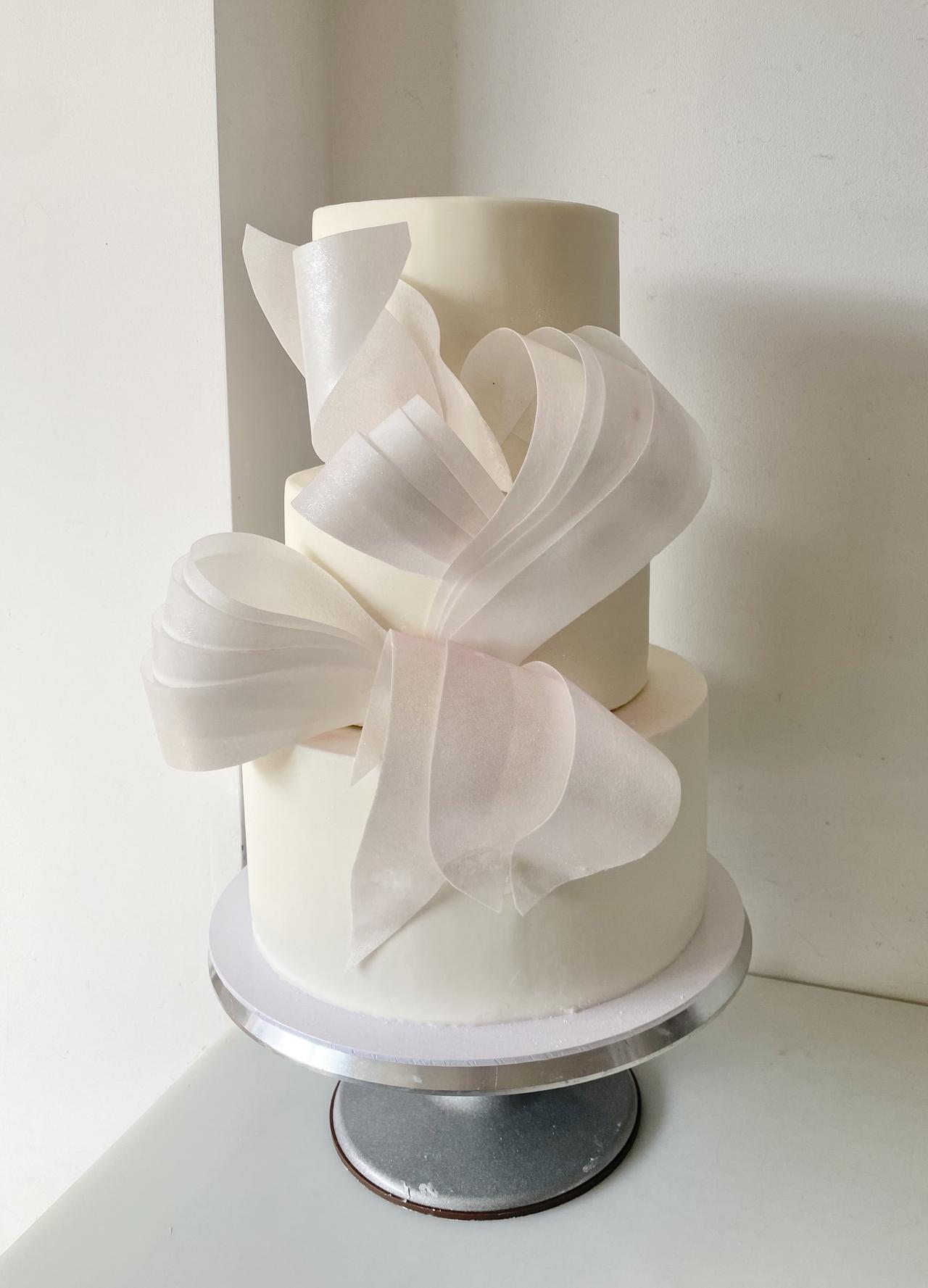 An all-white tiered wedding cake with sculptural decoration on the front.