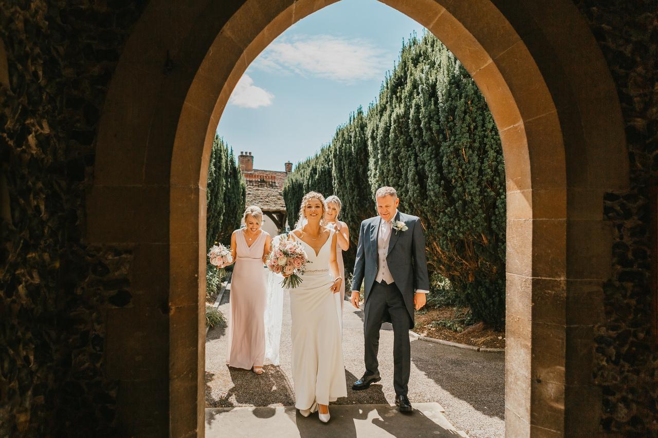 The bride approaches the church with her dad and bridesmaids