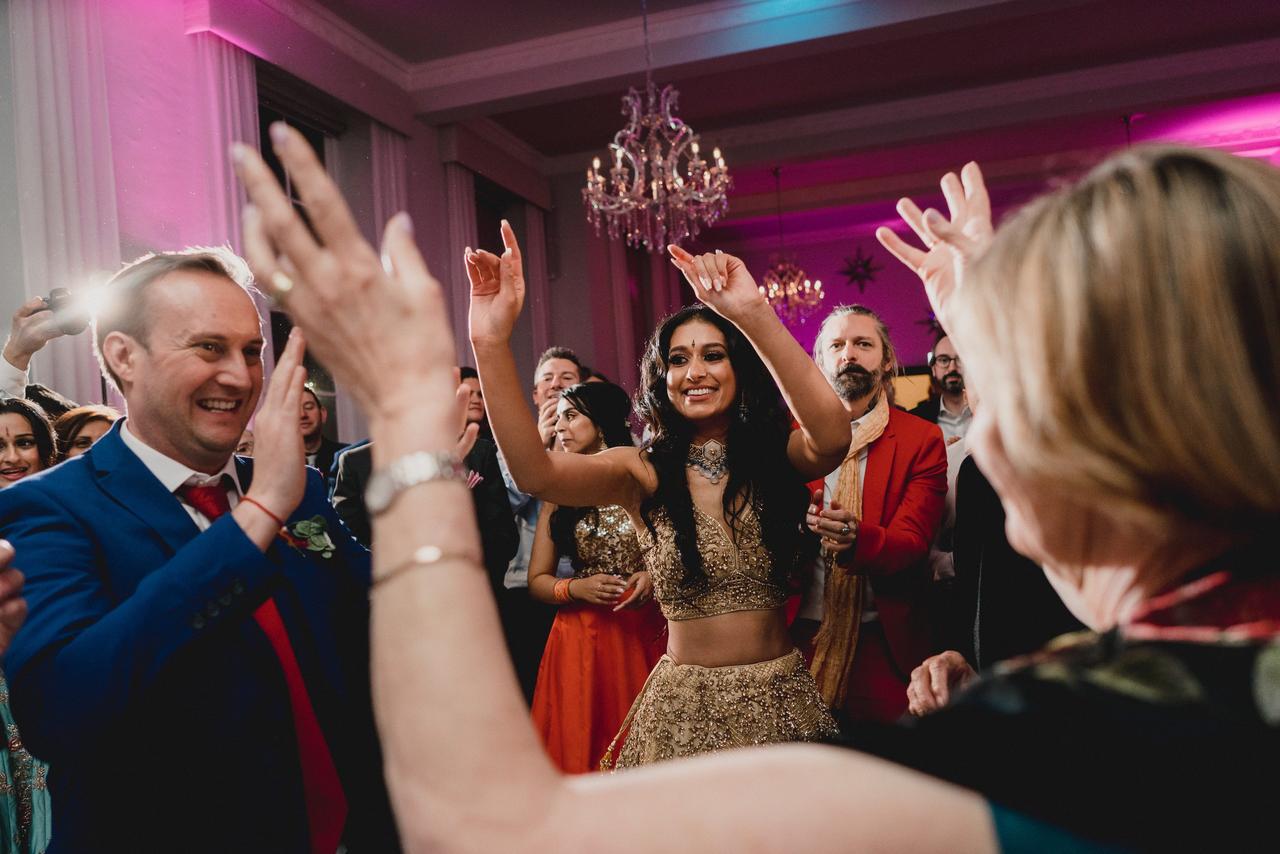 An Asian bride in traditional south asian attire dancing with her wedding guests.