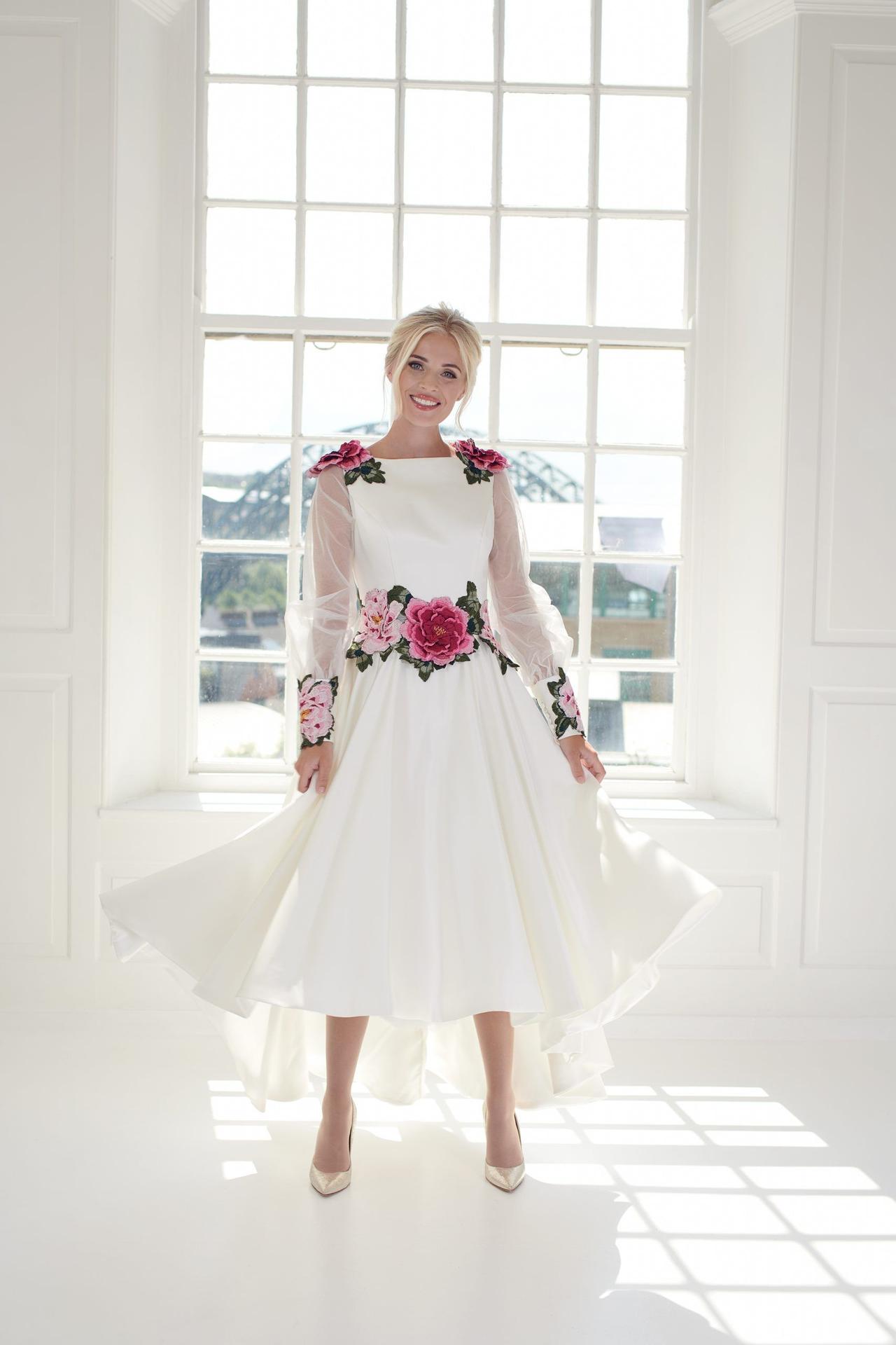 Model wearing a sheer long sleeved wedding dress with pink roses