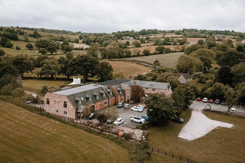 Aerial view of red brick farmhouse with car park surrounded by trees and fields