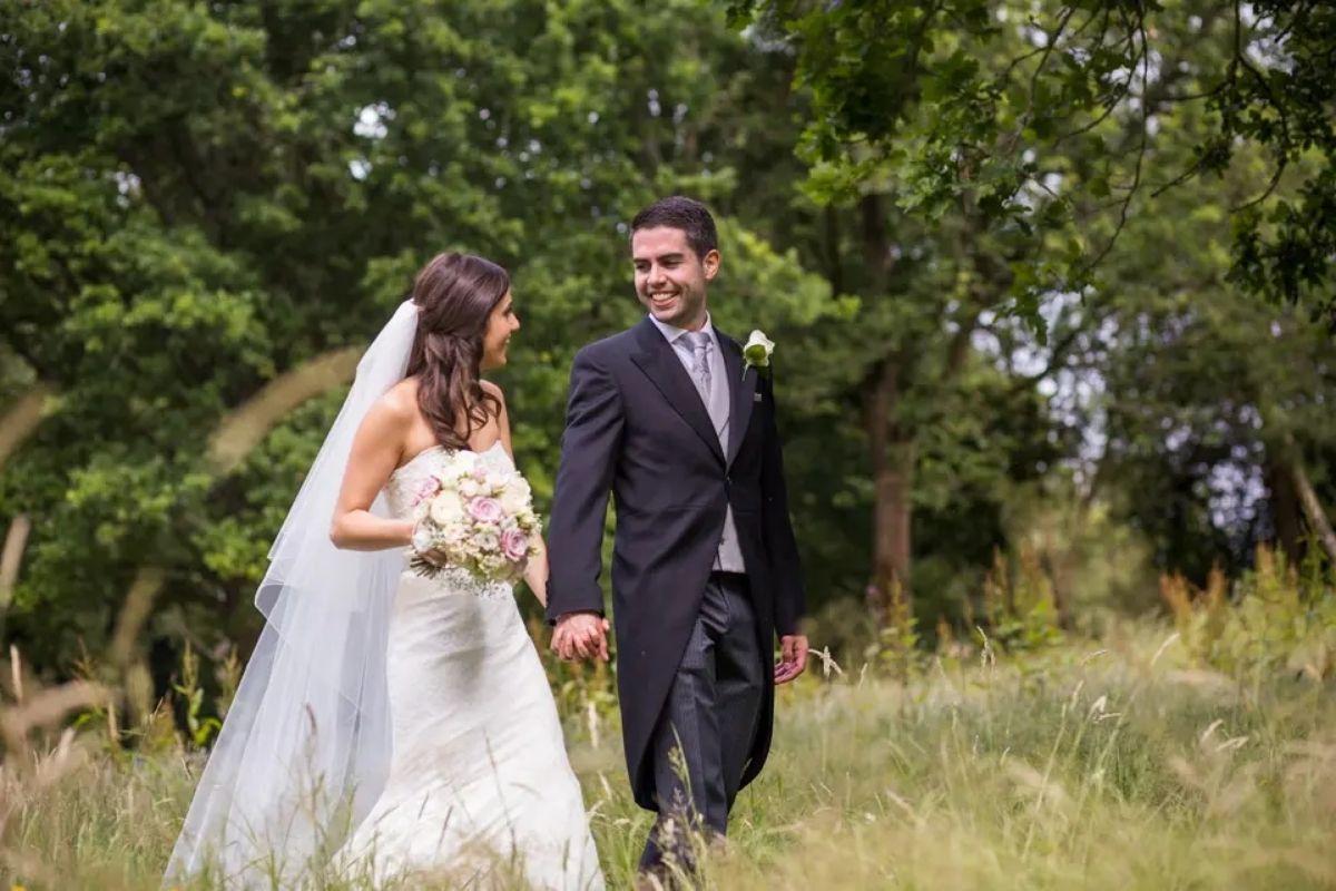 54 a bride and groom walking through a green grass field with trees in the background