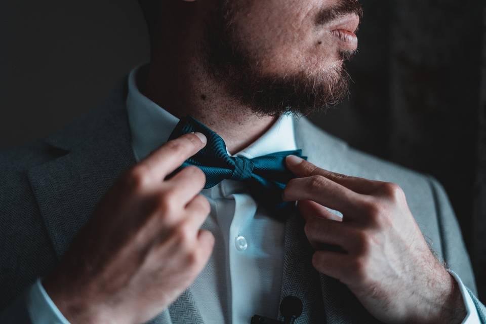 Man with a beard tying a bowtie in a grey suit