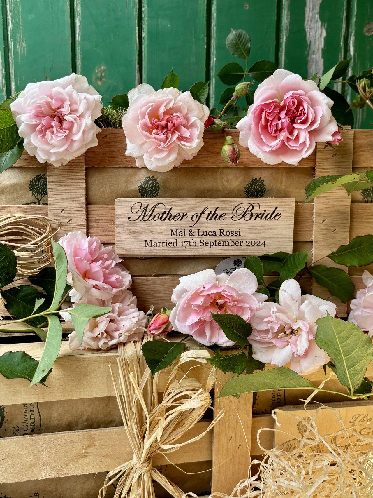 A wooden crate featuring a young rose plant and a personalised wooden plaque