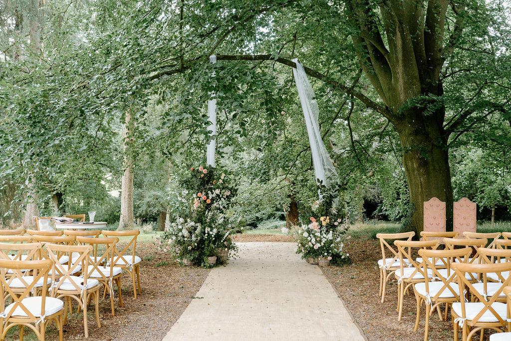 An outdoor aisle with white drapes hanging from the trees 