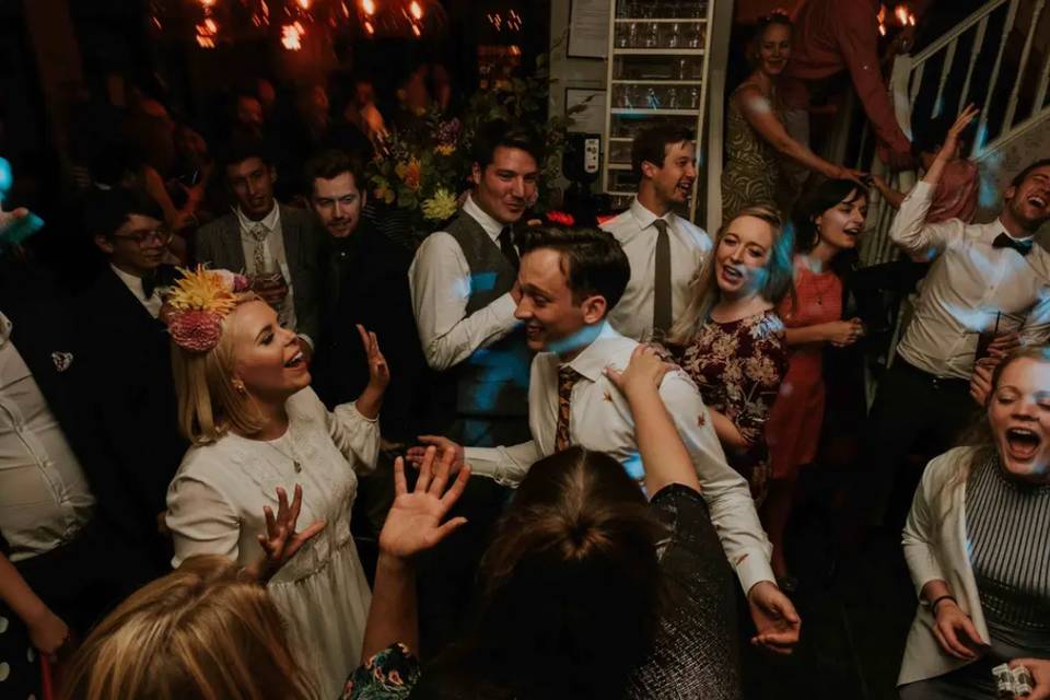 a bride, groom and their wedding guests dancing on the dancefloor at their wedding reception while listening to their wedding entertainment