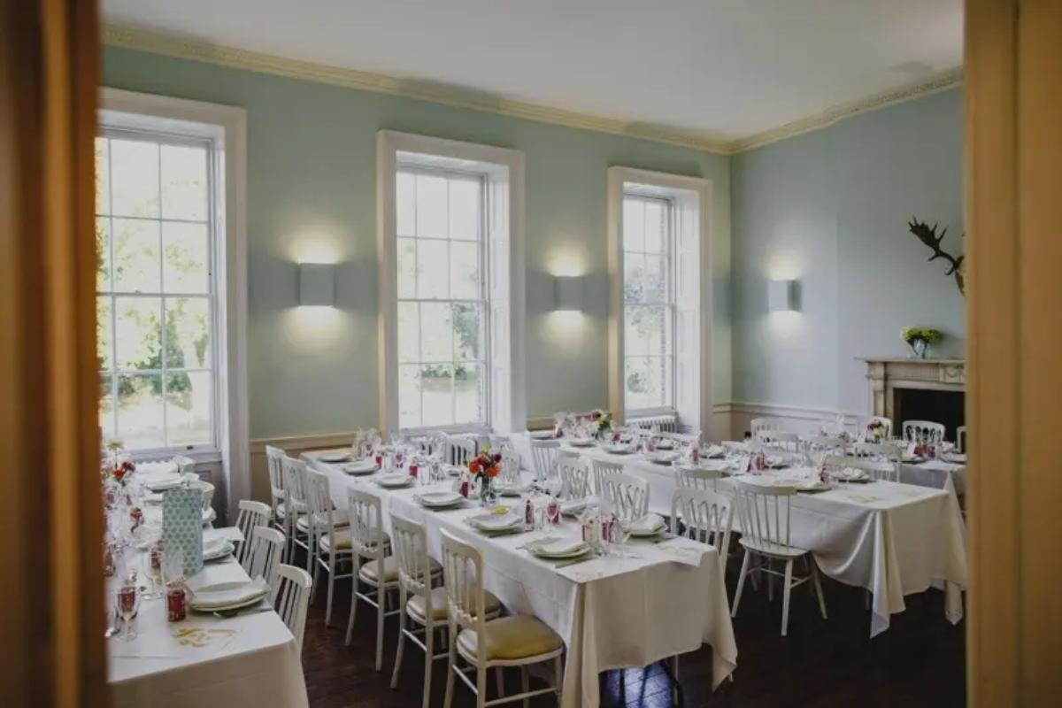  a dining room at clissold house set up for a wedding breakfast with three large windows next to each banquet table