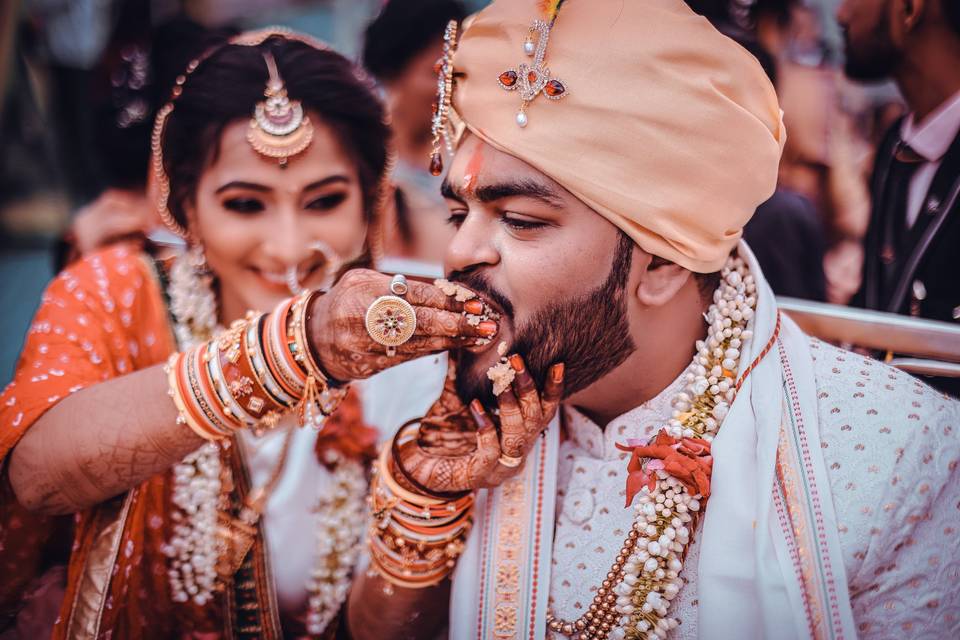 Bride with gorgeous bridal mehndi on hands and arms feeding her groom cake on their wedding day 
