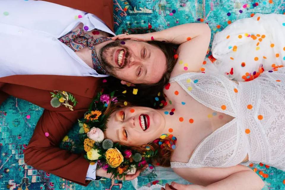 a couple lying with their heads next to each other surrounded by colourful confetti
