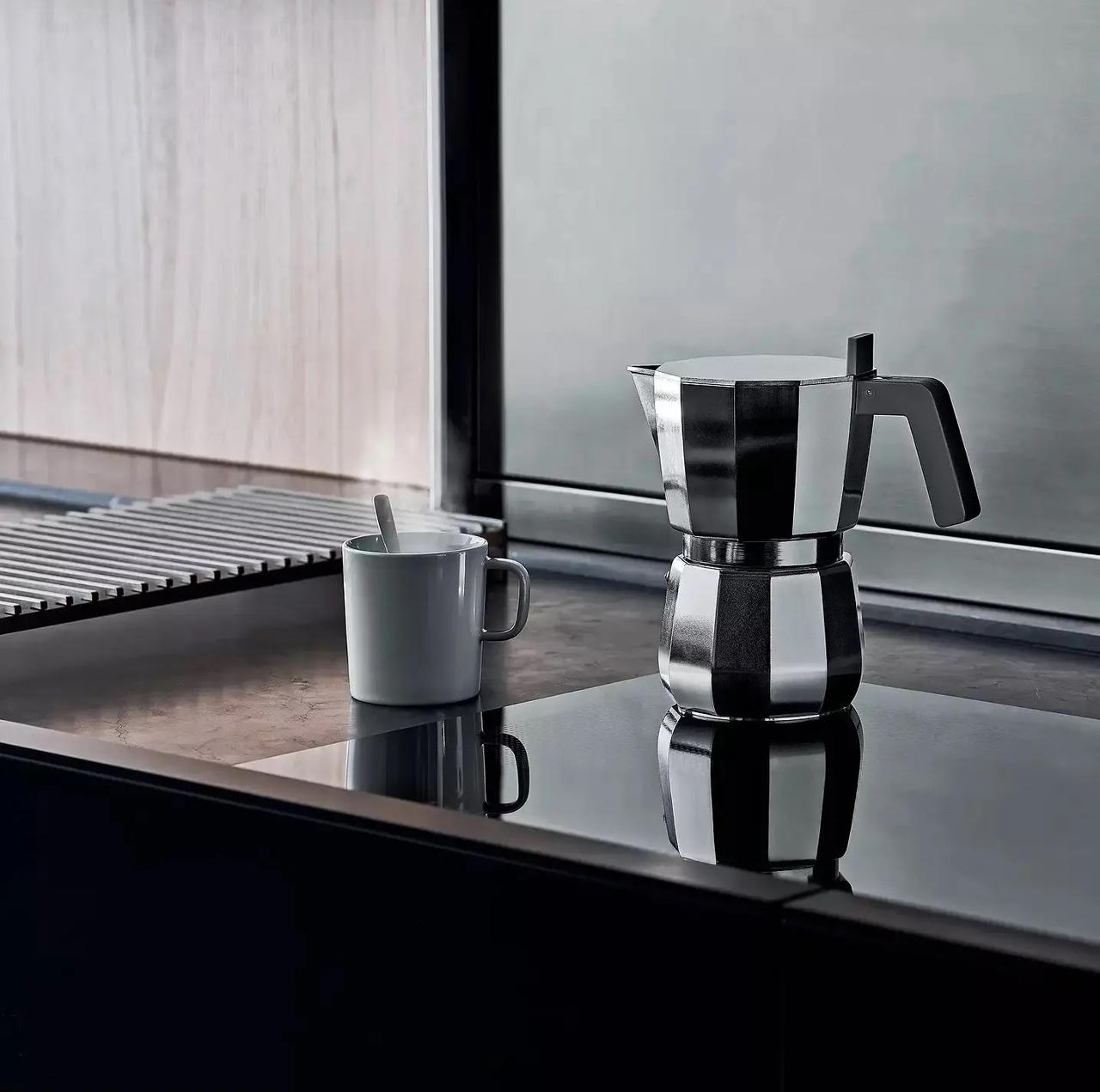 A stylish coffee pot made from stainless steel  and a cup pictured on the kitchen side. 