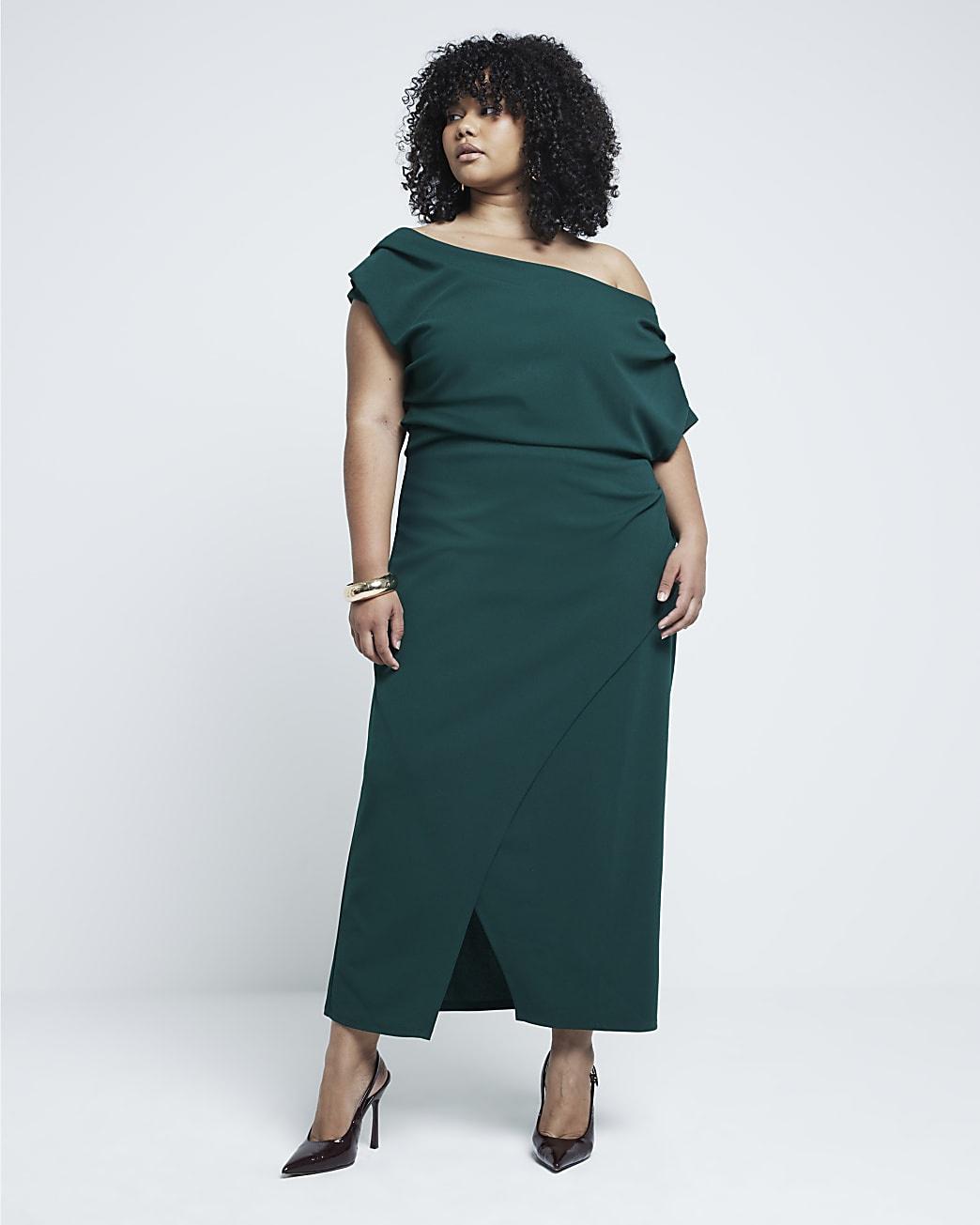a plus size wedding guest wearing a green off the shoulder dress with black heels.