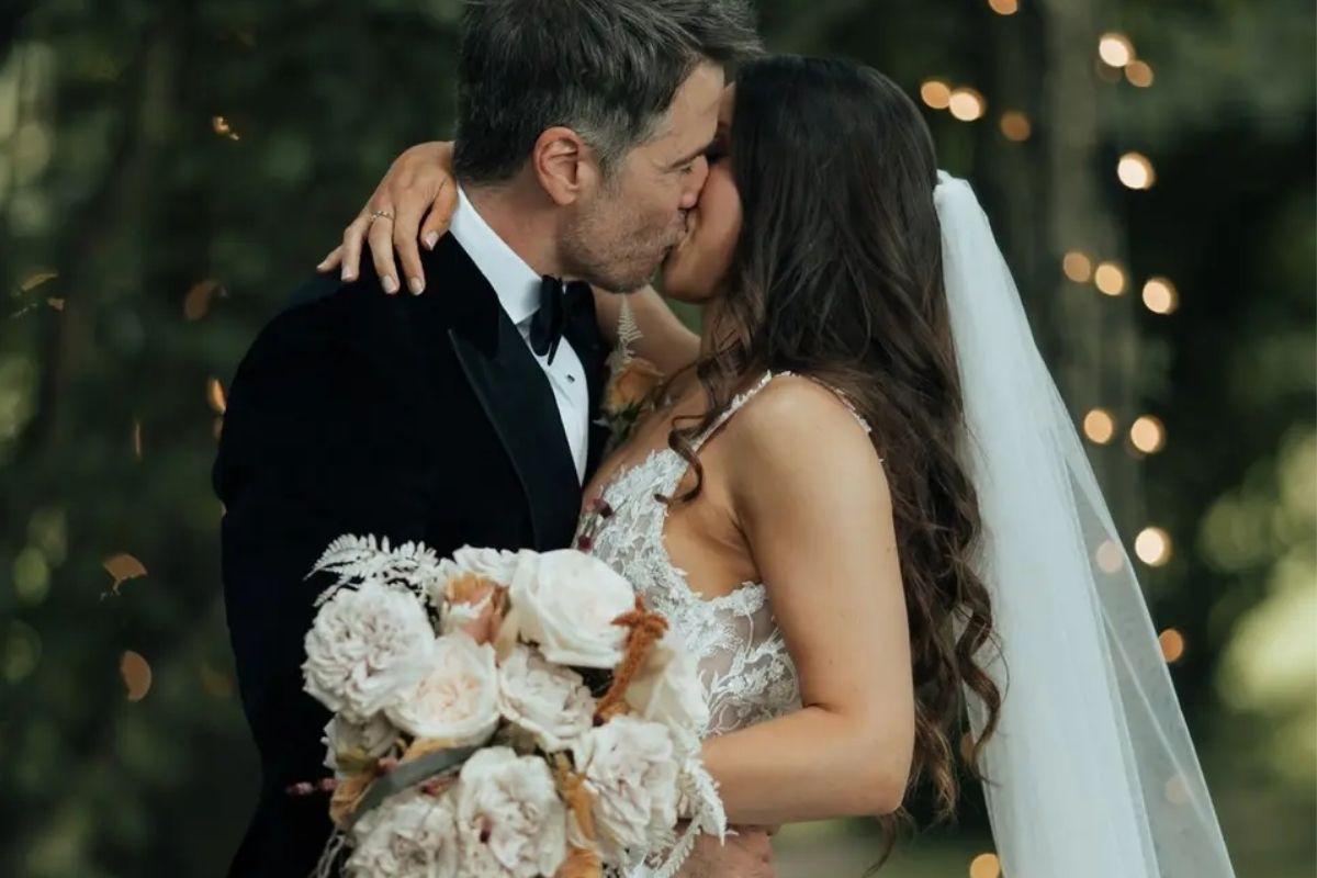 a bride with her arm around her groom kissing and holding her peach and white wedding bouquet