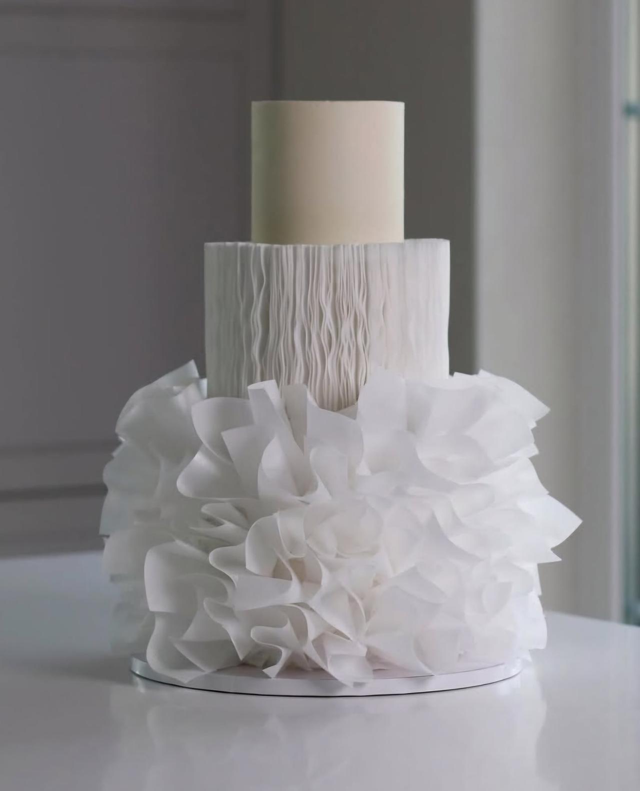 A white iced tiered wedding cake with ruffled and wafer detail.