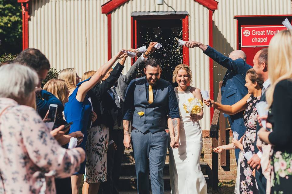 Man and woman exiting their wedding ceremony walking through confetti